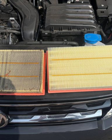 Two car air filters side by side, one dirty and one clean, with an engine in the background.