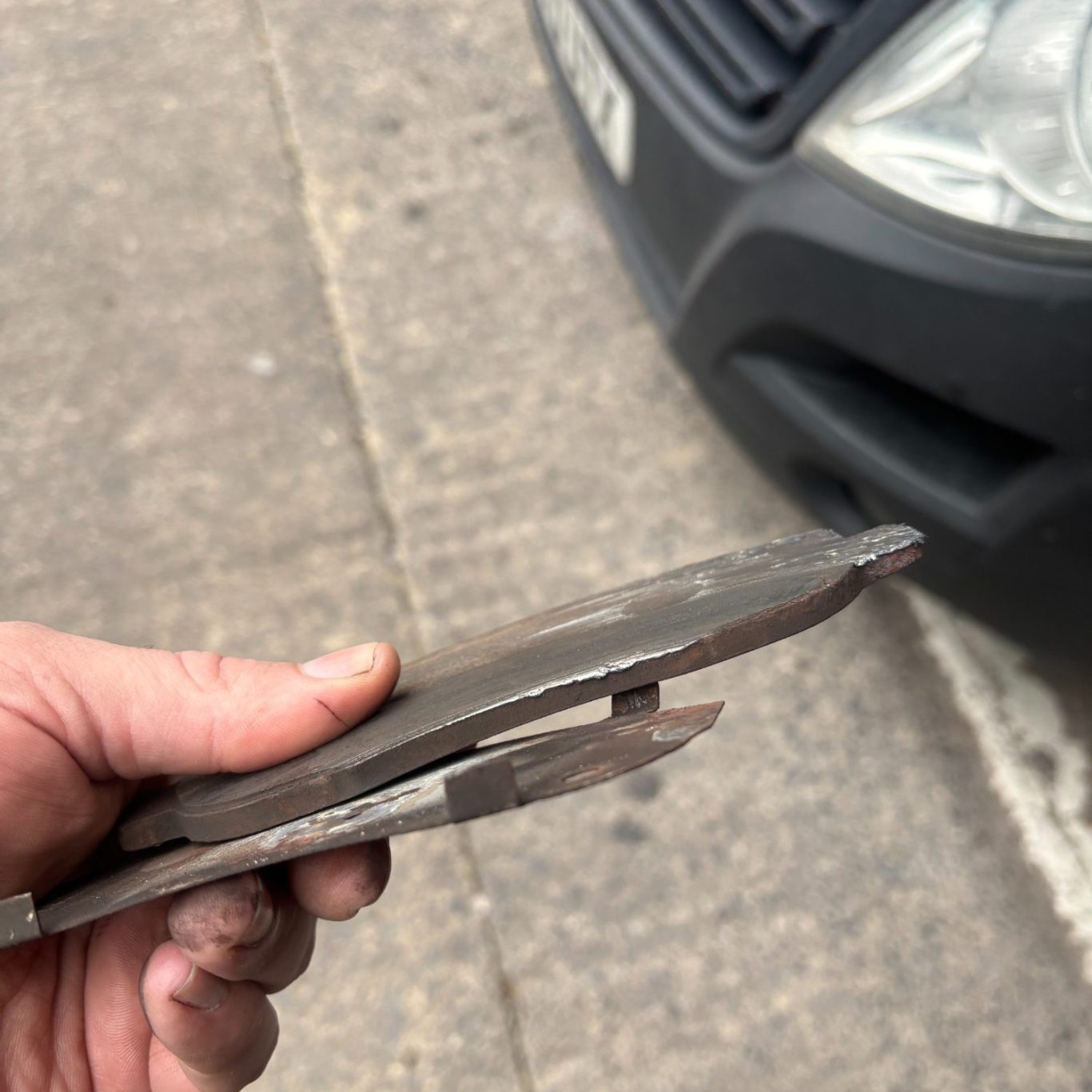 Repair A hand holding worn brake pads near a vehicle's front end.