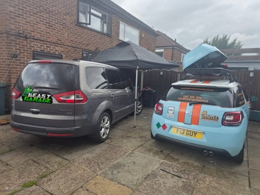 Two cars parked outside a house, one with a raised boot and a canopy nearby.
