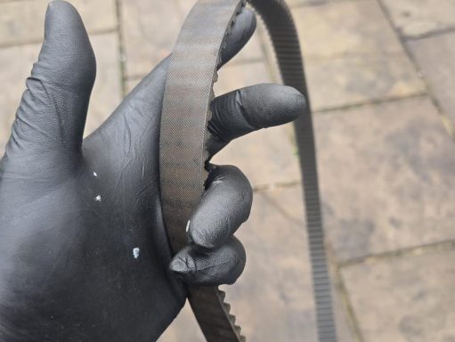 A person wearing a black glove holds a worn rubber belt.