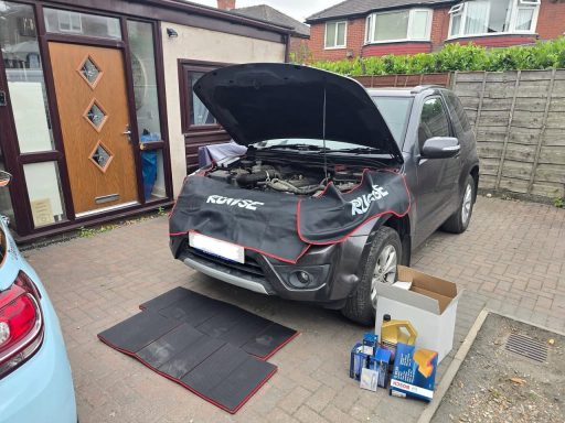 Black SUV with hood open, tools and equipment arranged on the ground nearby.